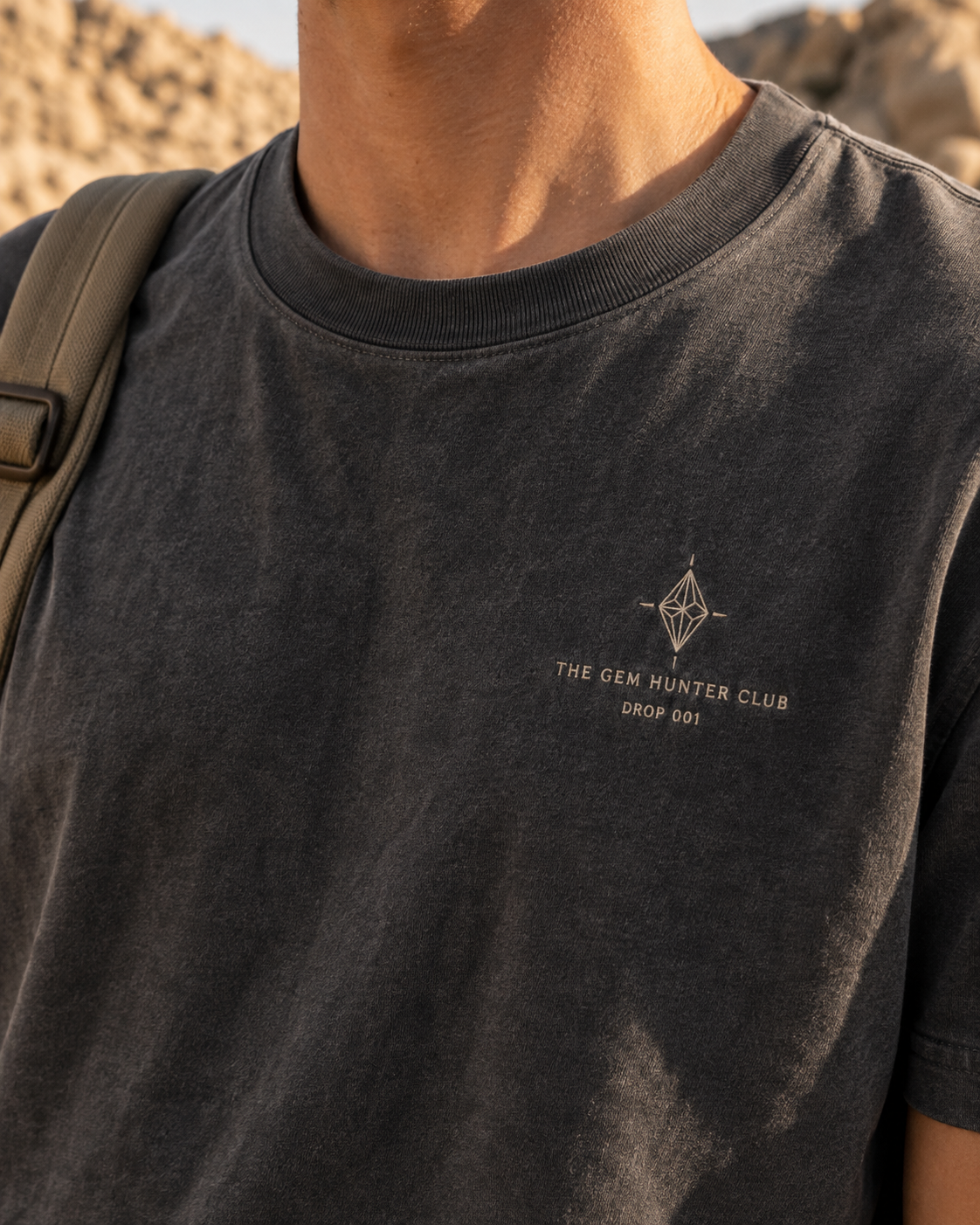 Proposed Founding Tee design: cropped front chest and ribbed collar in charcoal cotton, with a small embroidered mineral compass Club mark